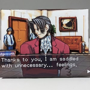 Puede incluir: Una ilustración digital de una escena del videojuego "Ace Attorney". El personaje, Edgeworth, lleva un traje rojo y una camisa blanca con un cuello con volantes. Está de pie en una sala de audiencias y dice: "Gracias a ti, estoy cargado de sentimientos... innecesarios."
