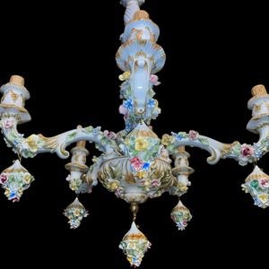 May include: A white porcelain chandelier with floral accents. The chandelier has five arms and is decorated with delicate flowers in shades of pink, yellow, and blue. The chandelier is a beautiful example of Italian craftsmanship.