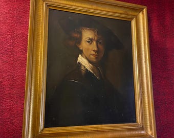 May include: A framed oil painting depicting a portrait of a person with reddish-brown hair wearing a dark hat, a white ruffled collar, and a dark garment. The artwork is enclosed in a wide, ornate gold-colored wooden frame with a smooth finish.