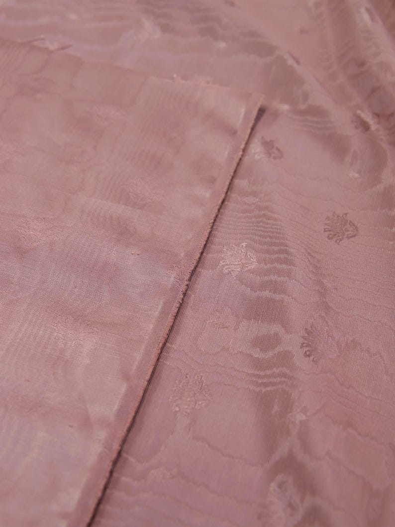 May include: A dusty rose fabric featuring a subtle, tonal jacquard pattern of small, repeating floral motifs. The material has a soft, semi-sheer quality with a visible weave and a slightly textured surface, showing a folded edge.