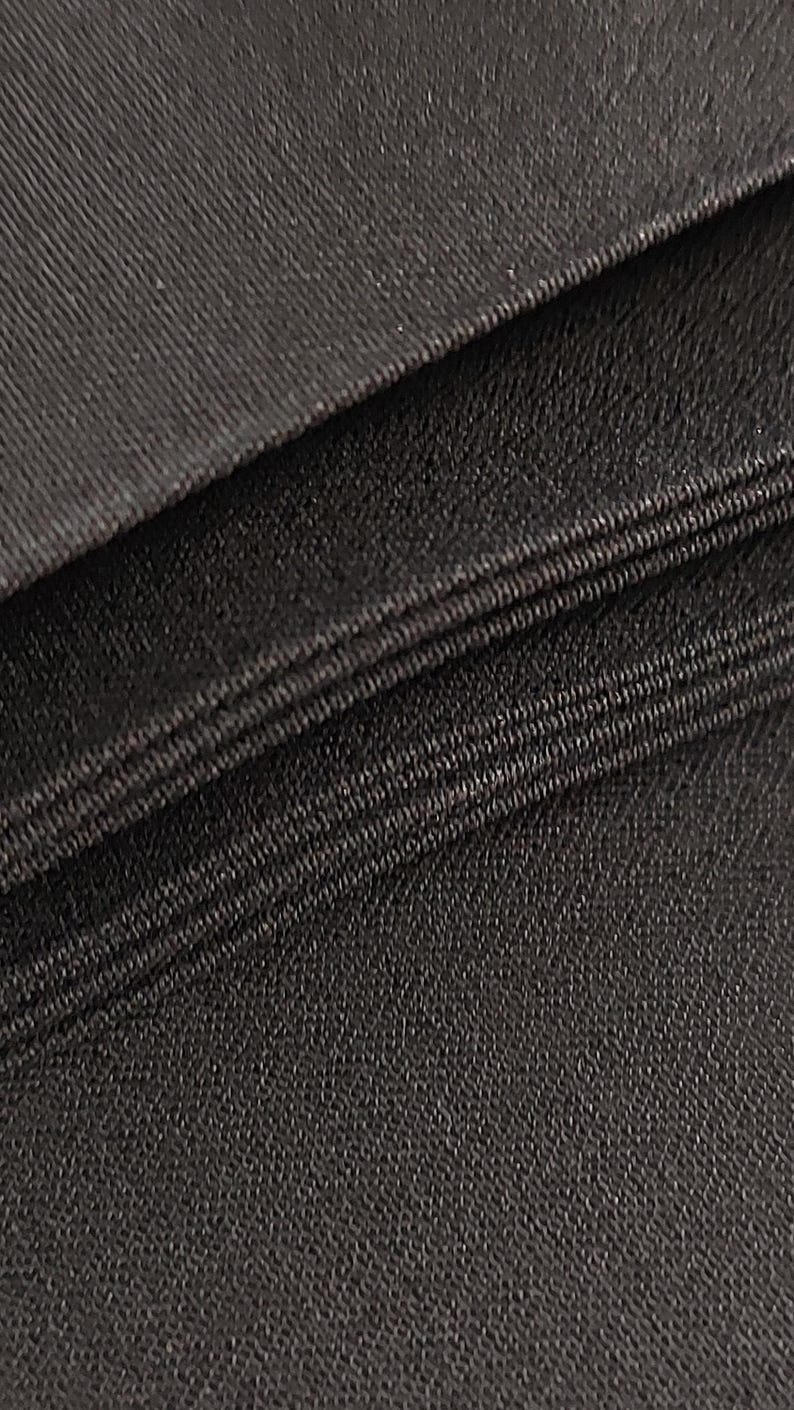 May include: Close-up of a black fabric with a textured weave. The fabric is folded in layers, showing the edges of each layer.