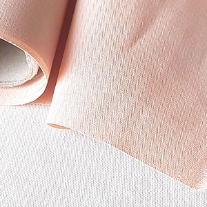 May include: A roll of pale pink fabric with a subtle herringbone pattern. The fabric is soft and has a slightly textured surface.