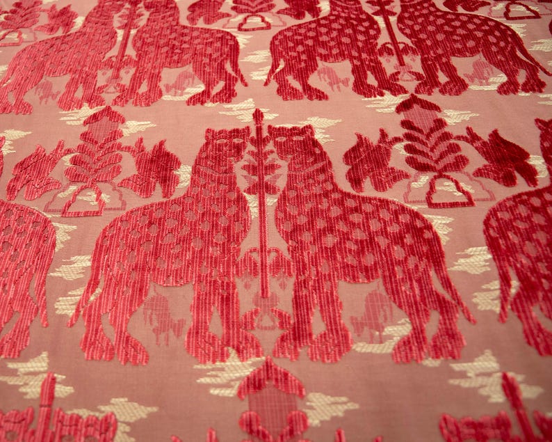 Pode incluir: Um tecido rosa com um padr&atilde;o repetido de animais estilizados vermelhos com manchas brancas. Os animais est&atilde;o em p&eacute; sobre um fundo branco com um desenho floral.