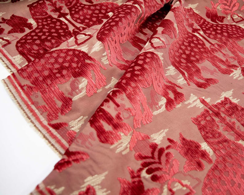 Pode incluir: Tecido de veludo vermelho com um padr&atilde;o repetido de figuras de animais estilizadas. O tecido tem um brilho sutil e uma superf&iacute;cie texturizada.