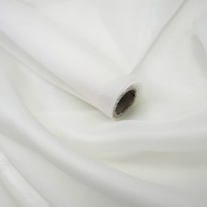 May include: A roll of sheer white fabric with a smooth, semi-transparent texture. The material is wrapped around a cylindrical cardboard core, creating soft, flowing folds and drapes that extend across the frame in a continuous, light-reflecting surface.