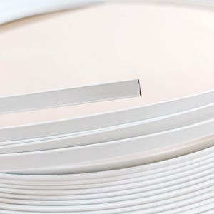 Op de afbeelding: Een close-up van een stapel witte, platte, rechthoekige sierlijsten. Eén stuk is gescheiden van de stapel en toont een schone, vierkante rand. De lijst lijkt gemaakt te zijn van een glad, stevig materiaal.