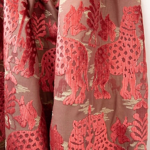 Pode incluir: Tecido de veludo vermelho com um padr&atilde;o em relevo de leopardos e folhagem. O tecido tem um brilho sutil e uma textura macia.