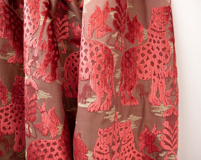 Pode incluir: Tecido de veludo vermelho com um padr&atilde;o em relevo de leopardos e folhagem. O tecido tem um brilho sutil e uma textura macia.