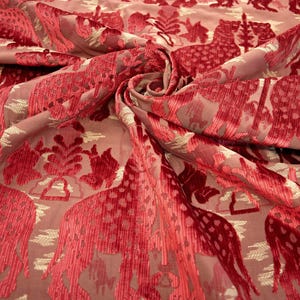 Pode incluir: Tecido de veludo vermelho com um padr&atilde;o repetido de girafas estilizadas e motivos florais. O tecido tem um brilho sutil e uma textura macia.
