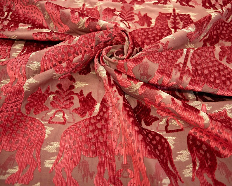 Pode incluir: Tecido de veludo vermelho com um padr&atilde;o repetido de girafas estilizadas e motivos florais. O tecido tem um brilho sutil e uma textura macia.