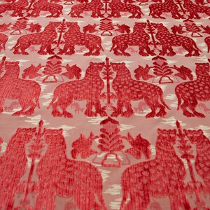Pode incluir: Tecido vermelho com um padr&atilde;o repetido de leopardos estilizados e &aacute;rvores. O tecido tem uma apar&ecirc;ncia texturizada, quase aveludada.