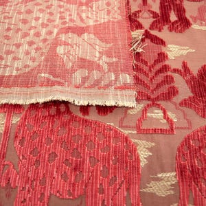 Pode incluir: Duas pe&ccedil;as de tecido vermelho com um padr&atilde;o de cor creme. A pe&ccedil;a superior tem um padr&atilde;o mais intrincado com um design floral. A pe&ccedil;a inferior tem um padr&atilde;o mais simples com um design geom&eacute;trico.