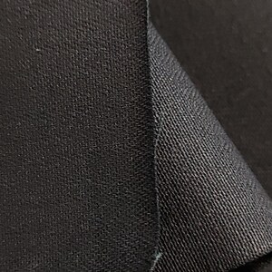 May include: Close-up of black fabric with a textured weave. The fabric is folded over on itself, showing the underside of the material.