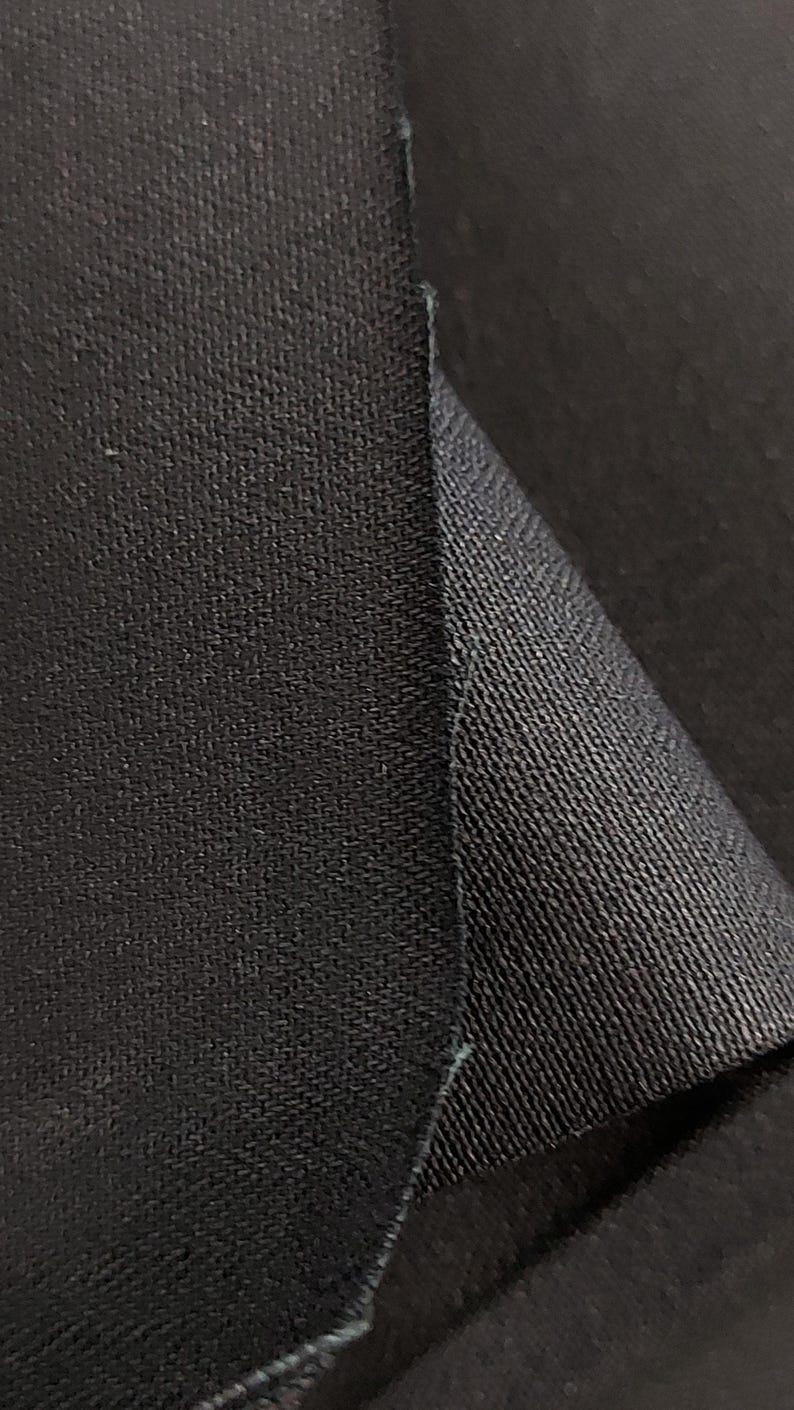 May include: Close-up of black fabric with a textured weave. The fabric is folded over on itself, showing the underside of the material.