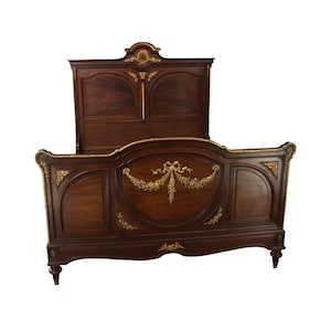 May include: A dark wood antique bed frame with ornate gold accents and a headboard with two panels. The bed frame has a curved design and decorative floral motifs.