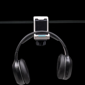 May include: A pair of black over-ear headphones hanging from a white and black plastic mount. The mount features a small horizontal blue accent line and a black adjustment knob on the underside, securely attached to a thin horizontal black bar.