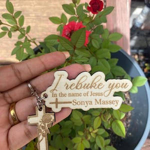 May include: Wooden keychain with a cross and a rose design. The keychain has the text "I rebuke you in the name of Jesus - Sonya Massey".