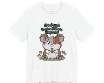 Peut inclure: T-shirt blanc avec un hamster de dessin animé tenant une collation, entouré de fleurs. Le texte "Rodent Rebellion Squad" est au-dessus du hamster. Le design utilise des couleurs marron, vert et blanc.