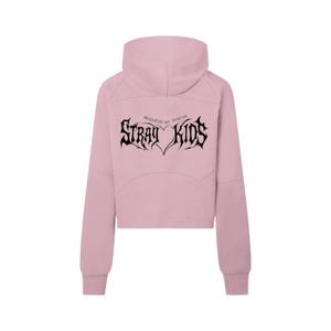 Może przedstawiać: Jasnoróżowa krótka bluza z kapturem z wysokim kołnierzem. Z tyłu bluzy znajduje się napis "STRAY KIDS" gotycką czcionką, nad nim "PRODUCED BY 3RACHA". Bluza ma długie rękawy i luźny krój.