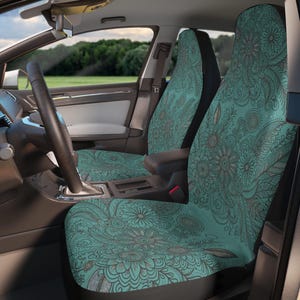 Puede incluir: Un par de fundas para asientos de coche con un fondo verde azulado y un patrón detallado de líneas gris oscuro de varias flores, hojas y elementos botánicos en espiral que cubren toda la superficie de los asientos delanteros y traseros.