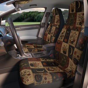 May include: A pair of car seat covers featuring a patchwork design with various illustrations including pumpkins, crescent moons, cauldrons, bats, and floral patterns in shades of orange, brown, black, and cream, installed on front vehicle seats.