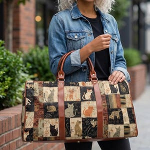 Pode incluir: Uma grande mala de viagem retangular com um design de patchwork com várias ilustrações de gatos em preto, laranja e cinza. A mala tem alças e correias de couro marrom. O fundo é uma mistura de quadrados bege, marrons e pretos.