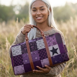 Puede incluir: Una bolsa de viaje de patchwork en tonos morados, con una gran estrella negra. La bolsa tiene asas y correas de cuero marrón. La bolsa es sostenida por una persona en un campo de hierba alta.
