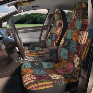 Op de afbeelding: Een paar autostoelhoezen met een veelkleurig patchworkontwerp met diverse bloemmotieven en geometrische patronen in tinten blauwgroen, bordeauxrood, mosterdgeel en roze, geïnstalleerd op de voorstoelen van een voertuiginterieur.