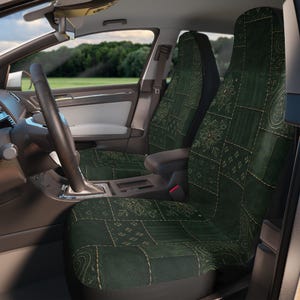 Peut inclure: Une paire de housses de siège auto vert foncé présentant un motif patchwork avec divers dessins floraux, cachemire et géométriques dans une teinte vert plus clair. Les housses sont installées sur les sièges avant d'un véhicule avec un volant noir.