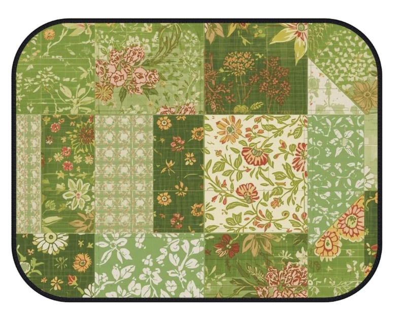 K&ouml;nnte beinhalten: Eine rechteckige Matte mit abgerundeten Ecken und schwarzem Rand, die ein Patchwork-Design aus verschiedenen gr&uuml;nen, wei&szlig;en und orangefarbenen Blumen- und Pflanzenmustern aufweist. Die Oberfl&auml;che zeigt ein Gitter aus Quadraten und Rechtecken.