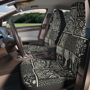Op de afbeelding: Zwarte en beige patroon autostoelhoezen. De hoezen hebben een patchwork ontwerp met paisley, bloemen en geometrische patronen. Het interieur van een auto is zichtbaar, inclusief het stuur en dashboard.