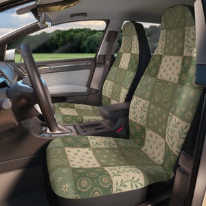 以下が含まれることがあります： 緑とクリーム色のパッチワークデザインの車のシートカバー。カバーには、正方形の中にさまざまな花柄とペイズリー柄があります。ハンドルとダッシュボードを備えた車のインテリアが見えます。