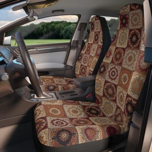 May include: Car seat covers with a patchwork design in shades of brown, beige, and burgundy. The pattern includes square motifs with floral and geometric elements. The covers are installed in a car interior, with a view of the steering wheel and outside scenery.