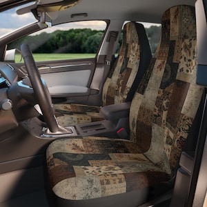 May include: A pair of car seat covers featuring a patchwork design with various earth-toned patterns in shades of brown, beige, and dark green. The covers are fitted over the front seats of a vehicle, displaying a detailed, multi-textured fabric print.