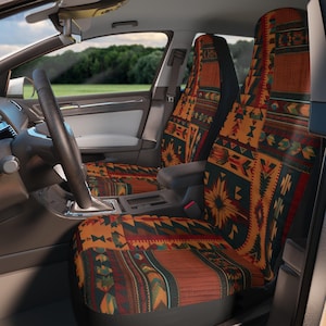 以下が含まれることがあります： 南西部のデザインのカーシートカバー。カバーは、オレンジ、赤、緑、茶色の幾何学模様、花、部族のモチーフの繰り返しパターンを特徴としています。ハンドルとダッシュボードが見える車のインテリアにカバーが取り付けられています。