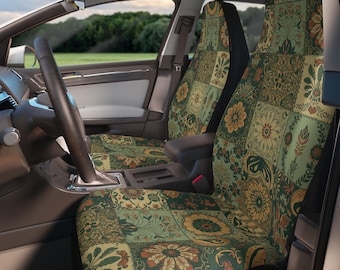 May include: A pair of car seat covers featuring a patchwork design of floral and botanical patterns in shades of sage green, mustard yellow, and burnt orange. The covers are fitted over the front seats of a vehicle with a black steering wheel.