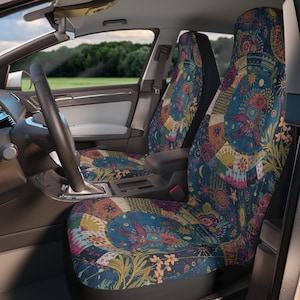 Op de afbeelding: Autostoelhoezen met een kleurrijk patchworkontwerp. De hoezen hebben een donkerblauwe achtergrond met bloemen-, hemelse en geometrische patronen in oranje, geel, roze en groen. Het interieur van een auto is zichtbaar.