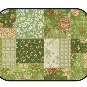 K&ouml;nnte beinhalten: Ein rechteckiges Platzset mit abgerundeten Ecken und schwarzem Rand, das ein Patchwork-Design aus verschiedenen gr&uuml;nen, wei&szlig;en und orangefarbenen Blumen- und Geometriemustern aufweist. Die Oberfl&auml;che zeigt ein Gitter mit botanischen Motiven.