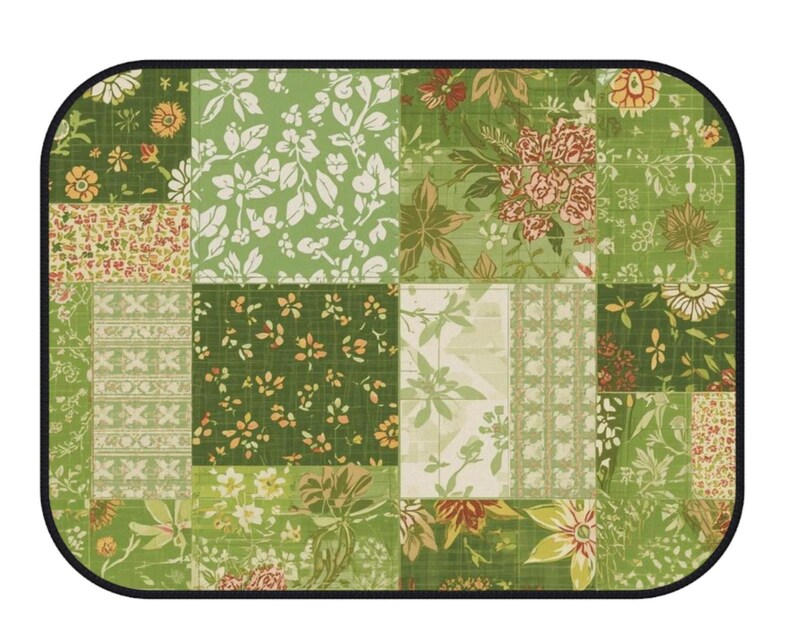 K&ouml;nnte beinhalten: Ein rechteckiges Platzset mit abgerundeten Ecken und schwarzem Rand, das ein Patchwork-Design aus verschiedenen gr&uuml;nen, wei&szlig;en und orangefarbenen Blumen- und Geometriemustern aufweist. Die Oberfl&auml;che zeigt ein Gitter mit botanischen Motiven.