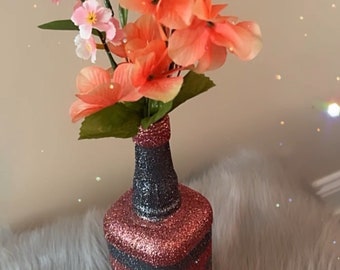 May include: A glass bottle vase with pink and black glitter stripes, holding a bouquet of pink and orange artificial flowers.