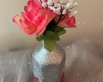 May include: A silver and pink glitter vase with a pink and white flower arrangement. The vase has a silver glitter top and a pink glitter bottom.