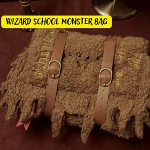 May include: A brown plush monster bag with two leather straps and the text "The Monster Book of Monsters" embroidered on the side.