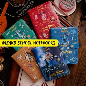 Puede incluir: Seis cuadernos temáticos de Harry Potter con diferentes escudos de casas y diseños. Los cuadernos están todos cerrados y presentan el texto "Harry Potter" en la portada.