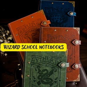 Peut inclure: Quatre cahiers reliés en cuir avec différents blasons de maisons du monde des sorciers. Les cahiers sont marron, vert, bleu et orange avec des accents dorés. Les blasons sont pour Gryffondor, Serpentard, Poufsouffle et Serdaigle.