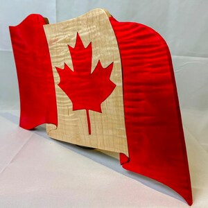Peut inclure: Un drapeau canadien en bois avec une feuille d'érable rouge sur fond blanc. Le drapeau est fait de bois d'érable et est peint en rouge et blanc.