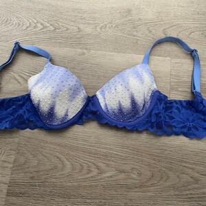 Op de afbeelding: Een blauwe en witte tie-dye bh met een kantversiering. De bh heeft een witte achtergrond met blauwe tie-dye patronen en is versierd met kleine witte kralen.