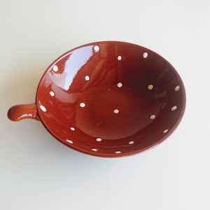 May include: A terracotta bowl with a white polka dot pattern and a handle. The bowl is empty and has a glossy finish.