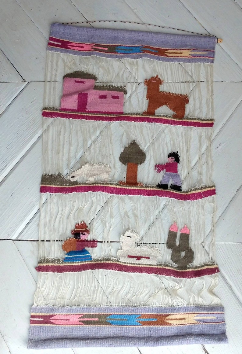 May include: A woven wall hanging with a colorful design featuring a house, a tree, a llama, a sheep, and two figures. The hanging is made of white yarn with red, pink, brown, green, and blue accents.