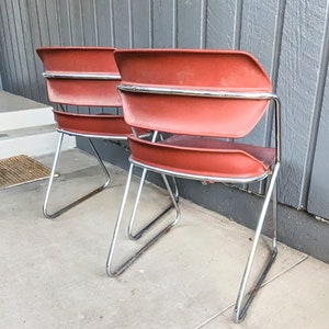 May include: Two red metal chairs with chrome frames. The chairs are facing away from the camera and are sitting on a concrete floor.