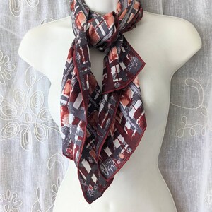 May include: A red, grey and white patterned silk scarf with a white "Jhn" signature in the corner.
